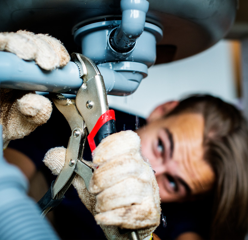 אינסטלטור מטפל בנזילה מתחת לכיור באמצעות מפתח צינורות